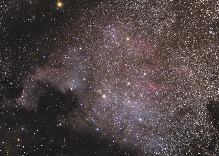 NGC 7000 — North America Nebula surrounded by dense Milky Way star fields and dark interstellar dust.